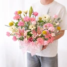 Pink lilies, gerberas, carnations, and yellow button mums in a white box with a pink bow.