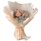Pink roses and dusty miller leaves arranged in a peach bouquet with a satin ribbon.