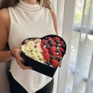 Heart-shaped box filled with strawberries, blueberries, and white flowers.