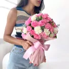 Woman in striped top and jeans holding pink and white carnation bouquet wrapped in pink paper with a pink bow.