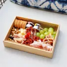 Charcuterie box with meats, cheeses, crackers, grapes, nuts, and jams on a light surface.