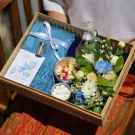 Songkran gift basket with blue scarf, flowers, perfume bottle, and small silver bowls of offerings.