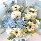 Blue hydrangeas, white roses, and gerbera daisies in a bouquet wrapped in blue and white paper.