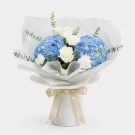 Bouquet of blue hydrangeas, white roses, white carnations, and eucalyptus, wrapped in white and blue paper.