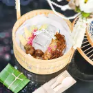 Bamboo basket filled with Thai Khao Chae dishes, bottle, and utensils.