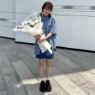Woman in denim outfit holding a bouquet of white roses, white carnations, blue hydrangeas, and eucalyptus.