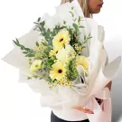 A bouquet of white gerbera daisies and roses wrapped in white paper and tied with a white ribbon.