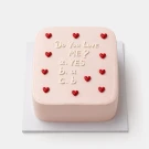 Pale pink frosted cake with red hearts and "Do you love ME? a. YES b. a c. b" in white icing.