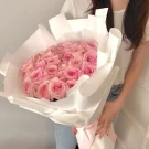 Bouquet of 30 pink roses beautifully wrapped in white paper, held by a person.
