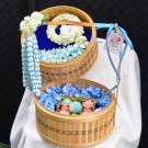 A 2-tier traditional bamboo basket set featuring a delicate garland and artisanal Thai desserts on fresh floral beds