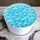 Round white box filled with sky blue artificial roses, each with a diamond accent.