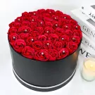 Black round box filled with red roses adorned with diamonds.