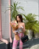 Woman in white tube top and pink plaid pants holds a bouquet of pink and white flowers.
