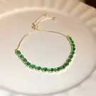 Gold chain bracelet with small, emerald-green oval gemstones and adjustable clasp.