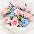 Pink roses and blue hydrangeas bouquet with white wrapping and ribbon.