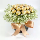 Ferrero Rocher chocolates in a round box with white gypsophila and a tan ribbon bow.