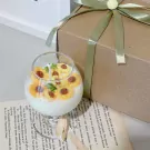 Sunflower scented candle in a wine glass, topped with tiny sunflower candles. Gift box in background.