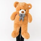 Fluffy yellow teddy bear wearing a brown and white checkered bow, sitting on a table.