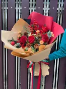 Christmas bouquet of red roses, berries, pine cones, and eucalyptus, wrapped in brown paper with a red and green ribbon.