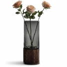Three light pink roses in a grey glass vase with a dark wood base.