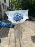 Blue hydrangeas in a white paper bouquet with a cream ribbon.