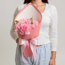 Pink carnation bouquet with a pink ribbon bow, held by a person in a white top.