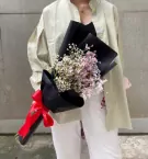 Woman holding a bouquet of white and pink dried limonium flowers, wrapped in black paper and tied with a red bow.