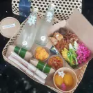 Khao Chae set with rice, side dishes, jasmine water bottles, and dessert in a woven basket.
