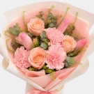 Peach and pink roses, carnations, and tulips in a bouquet, wrapped in white paper with a pink ribbon.