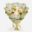 A bouquet of white and pink roses, daisies, and greenery wrapped in pale green paper, tied with a cream ribbon.