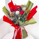 Christmas bouquet with red roses, white ping pong balls, pine cones, pine branches, and red berries.