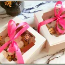 Two white gift boxes filled with chocolate chip cookies, tied with pink ribbons, on a marble surface.