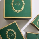 Green Le Souri chocolate boxes with gold trim and ornate emblem, presented on a white surface.