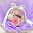 Graduation balloon bouquet with teddy bear, pink gerbera daisy, white mums, and small daisies, wrapped in purple paper.