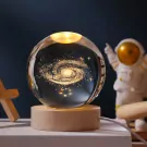 A galaxy etched inside a crystal ball on a wooden base, with an astronaut figurine in the background.