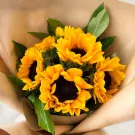A bouquet of bright yellow sunflowers wrapped in brown paper.