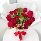 A large bouquet of 24 red roses and baby's breath, wrapped in white paper and tied with a red ribbon.