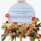 Floral stand with red anthuriums, pink roses, and greenery on a congratulatory sign.