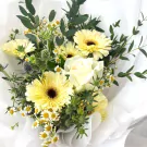 Bouquet of yellow gerbera daisies, white roses, small white daisies, and thistles, accented with eucalyptus leaves.