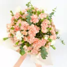Peach and white carnation bouquet with eucalyptus in a vase, tied with a peach ribbon.