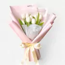 White tulips in a light pink paper bouquet tied with a satin ribbon bow.