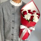 Bouquet of red roses and white carnations in red wrapping with a white bow.