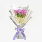 Purple tulips in white wrapping paper tied with a lavender ribbon.