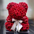A teddy bear made of red roses, tied with a ribbon and gift tag.