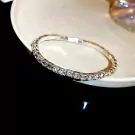 Close-up of a silver tennis bracelet with clear, square-cut stones on a white dish.