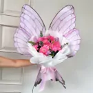 A bouquet of pink flowers and tulips wrapped in white paper with large purple butterfly wings behind it.