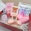 Pink gift box with perfume, makeup remover, teddy bear card, and heart-shaped plush.