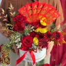 Festive red Chinese New Year flower box with roses, gerberas, gold ingots, and red envelopes.