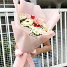 A bouquet of pink and white gerberas and red carnations wrapped in pale pink paper.