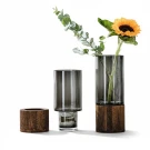 Two glass vases with wooden bases on a white background, one holding a sunflower and greenery.